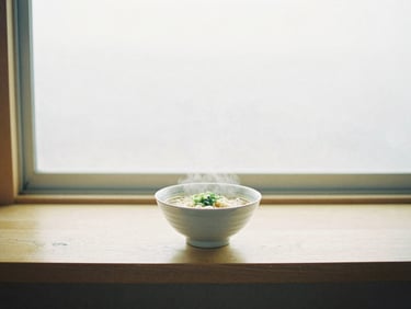 A single steaming bowl of ramen on a light wooden counter, soft diffused window light, minimalist table setting, pastel tones, 35mm film aesthetic.