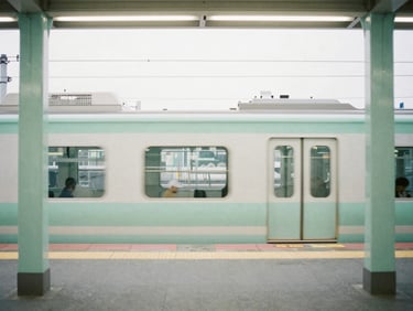 A quiet, empty train platform in Tokyo during overcast morning daylight, soft pastel green pillars, clean lines, minimalist composition, 35mm film aesthetic.