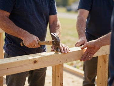 Close-up of volunteers hands holding a hammer and securing a new wooden beam during a community home rebuilding project in Ohio, warm daylight.
