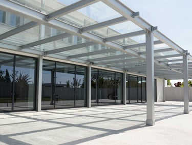 A modern outdoor pergola with integrated structural glass roof panels, clean steel frame, sharp architectural shadows.