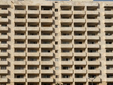 Straight-on elevation photograph of a completed eight-storey apartment tower in Amman, uniform balcony grid, natural midday light, full facade visible from street level
