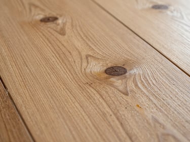 Extreme close-up of a reclaimed pine floor after sanding and oil finish, knots and grain pattern in full detail, tungsten sidelight emphasizing surface texture, no styling