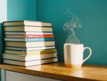 A cozy reading nook with a bright teal wall, a stack of colorful books, and a steaming mug, warm morning light.