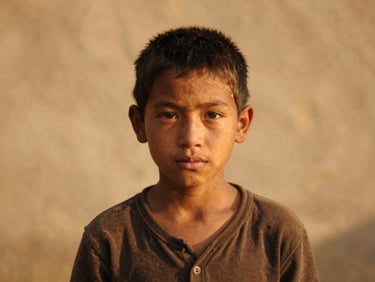 Dignified portrait of a young orphan boy looking directly at the camera with hope, warm golden-hour outdoor light