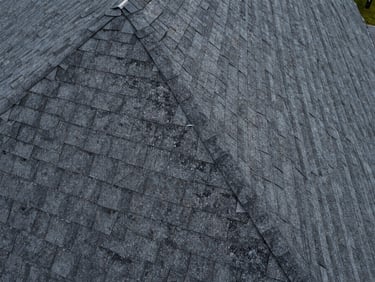 Close aerial of a residential asphalt shingle rooftop, granule wear and flashing detail visible, overcast diffused daylight eliminating harsh shadows, drone framing tight to roofline