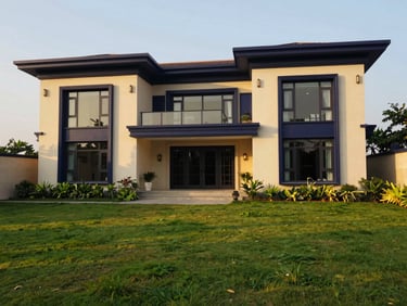 Wide-angle view of a modern luxury villa facade in India, golden hour sunlight, lush green landscaping, deep navy and champagne accents, 35mm