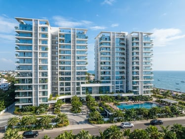 Wide-angle architectural photography of a premium modern apartment building exterior in Kakinada under bright, clear coastal daylight, crisp white facades and soft blue glass accents.