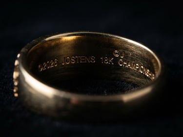 Macro photography of the official 2026 Championship Ring hallmark engraved inside the 18k gold band, dramatic low-key chiaroscuro lighting, metallic reflections against deep black background