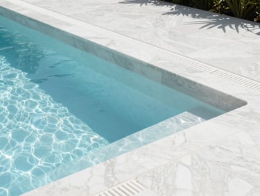 Architectural photograph of a renovated luxury pool, showing pristine new white marble plaster finish and modern overflow grates, bright daylight