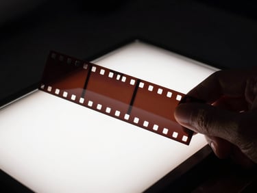 Macro shot of physical celluloid film strip held up against a soft glowing light table in a dark room