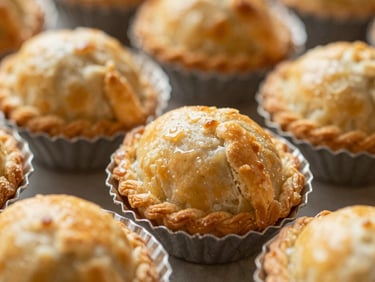 Close-up of golden-brown baked empadas in their small tin molds, flaky pastry texture, warm lighting