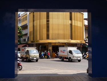 Busy urban street in a Vietnamese city, delivery trucks, local businesses, dynamic, natural light, warm cast, deep navy and warm gold tones, sharp focus, architectural framing, 35mm.