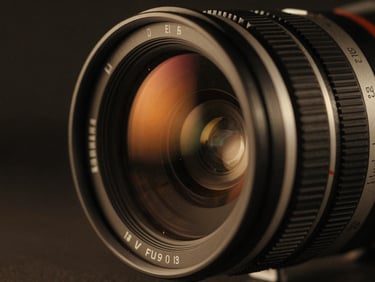 Extreme close-up of an anamorphic camera lens, dramatic low-key studio lighting with warm orange reflections, deep shadows, 35mm film texture.