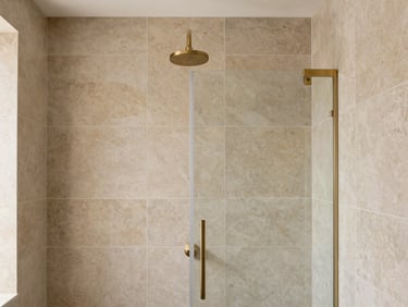 A luxury bathroom walk-in shower with large-format warm stone tiles, a brushed gold shower head, and flawless grouting lines, soft daylight, 35mm