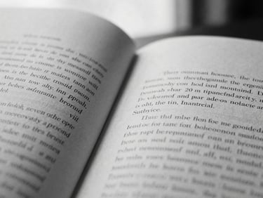 A close-up macro photograph of open book pages, elegant serif typography on textured paper, high-contrast shadow across the center fold, desaturated black and white tones