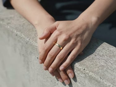 A close-up of hands resting on a brutalist concrete ledge, soft shadow falling across a gold wedding band, sharp natural light, minimal composition.
