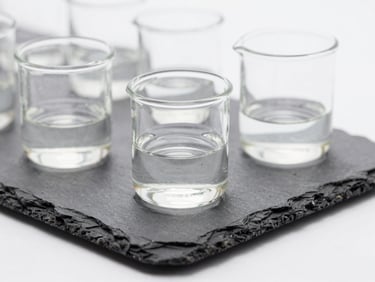 Close-up macro photography of sterile laboratory glassware containing clear active formulation, clean clinical daylight, sharp focus, slate and white tones.