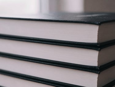Stack of three freshly printed books with crisp black spines, matte texture, close-up.