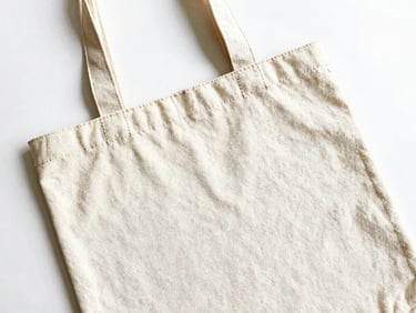 Bright high-key product photography of a custom canvas tote bag flat-lay showing precise stitching details on a clean white background, 50mm