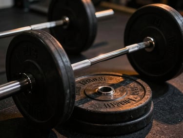Dramatic athletic photography, high-contrast gym lighting, a close-up of knurled barbells and weight plates in deep shadows with warm amber accents, 35mm lens