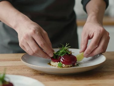 Close-up of hands carefully plating a gourmet dish in a rustic Scandinavian kitchen, soft side-light, rich crimson and forest green tones, shallow depth of field