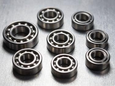 Close-up detail of precision engineering components — bearings, seals, and fasteners arranged on a brushed aluminum surface, studio strobe lighting from above, sharp metallic reflections