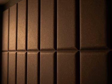 Close-up of discreetly integrated acoustic wall paneling in a luxury home cinema, warm ambient light, deep shadows, rich bronze and charcoal tones.