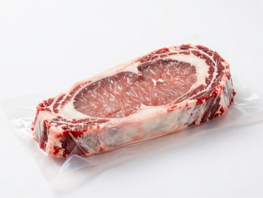 Vacuum-sealed raw beef ribeye steak on a sterile white surface, bright high-key lighting, macro shot.