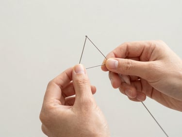 Close-up of hands meticulously weaving thin metal wire into a complex structural armature, bright natural daylight, clean neutral backdrop, sharp focus.