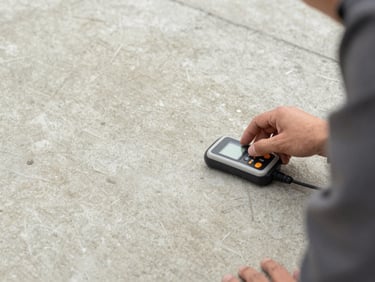 Close-up of a professional technician measuring concrete floor moisture with a digital device, precise hand movement, neutral mineral gray tones