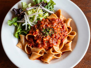 Overhead shot of a vibrant bowl of fresh pasta with rich sauce and a side of crisp salad, warm overhead casual restaurant lighting, saturated reds and creams, rich contrast, 50mm lens, shallow depth of field