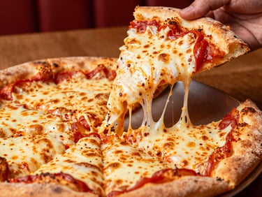 Close-up of a hand pulling a slice of California-style pizza with abundant cheese pull, warm overhead casual restaurant lighting, saturated reds and creams, rich contrast, 50mm lens, shallow depth of field