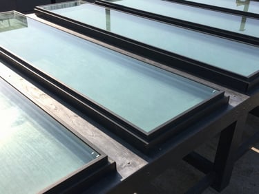 Close-up of industrial laminated glass panels framed in heavy duty black aluminum, bright natural daylight casting sharp structural lines, architectural photography style