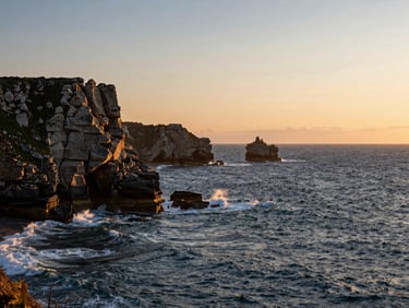 Dramatic coastal cliffs of Brittany at sunset, warm light hitting the ocean waves, peaceful atmosphere