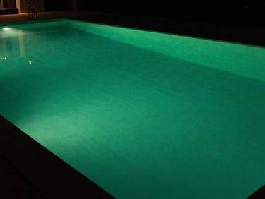 Dark architectural swimming pool with subtle green underwater lighting, clean lines, high-contrast, luxury estate setting, 35mm lens