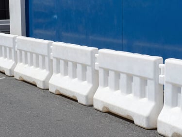 Crisp eye-level shot of a neat row of hot-dip galvanised barriers deployed along a New Zealand urban street, flat feet resting on asphalt, bright daylight