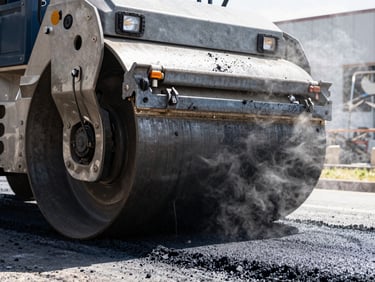 Heavy-duty asphalt roller compacting hot black asphalt under bright sun, steam rising, raw industrial texture, 35mm