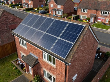 Overhead drone shot of a semi-detached UK home with CBG Solar panels installed across the rear roof slope, suburban street visible below, soft overcast daylight, system clearly operational