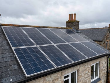 Wide shot of solar panels installed on a grey-slate UK terraced house roof, overcast British sky, surrounding rooftops visible in the background