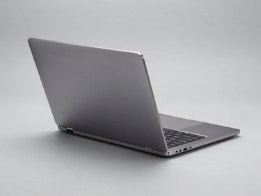 Tight three-quarter angle shot of a closed laptop on a plain light gray surface, showing the aluminum lid and hinge detail under even diffused studio lighting, no reflections, clean product photography