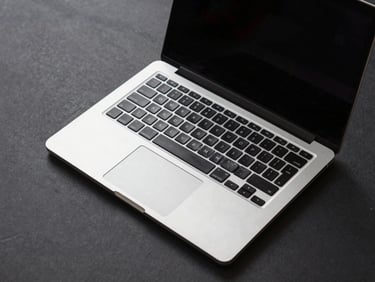 Overhead studio shot of a 15-inch business laptop open at 45 degrees on a charcoal surface, keyboard and trackpad visible, clinical even lighting, no shadows
