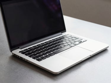 Close-up three-quarter angle of a business laptop open on a clean steel-gray desk, keyboard and screen both visible, screen displaying a plain dark interface, even ambient studio lighting, no shadows, full product body in frame showing port selection along the sides