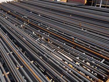 Wide-angle shot of a steel rebar cage being assembled on a construction site, sharp daylight, high contrast, charcoal and orange tones, with a focus on the structural integrity.