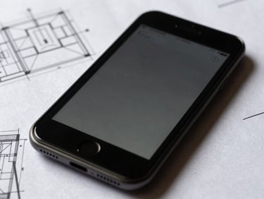 Crisp high-contrast photograph of a mobile interface displayed on a matte screen, surrounded by physical blueprint sheets