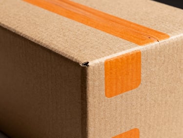 High-contrast studio photograph of a premium cardboard packaging box with sharp die-cut edges and safety-orange screen print