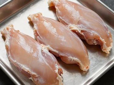 Overhead close-up of raw chicken breast portions arranged on a clean stainless tray under north-facing studio light — showing natural pale color, clean surface, no styling