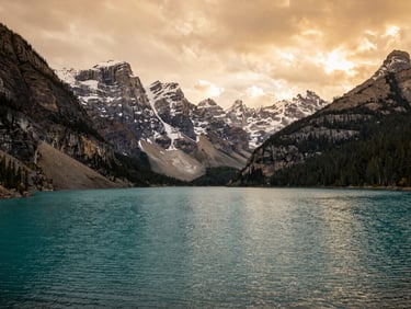 Wide panoramic shot of Banff National Park at golden hour, turquoise lake in the foreground, snow-capped Rockies in the background, warm amber light, no people — the landscape as it looks when you first arrive, not a postcard crop