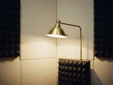 A quiet, minimalist recording booth with acoustic panels and a warm brass reading lamp lit.