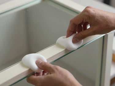 Close-up of hands applying thick protective foam corners and stretch film to a fragile glass mirror frame