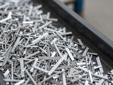 Macro overhead shot of shredded clean aluminum grains on a dark conveyor belt under sharp warehouse lighting.